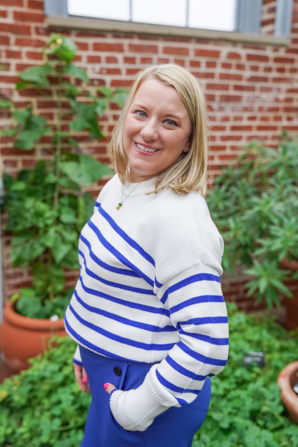 blonde woman in a striped sweater standing amongst green plants Katheryn Barton LPC Kirkwood MO Uplift and Connect Counseling